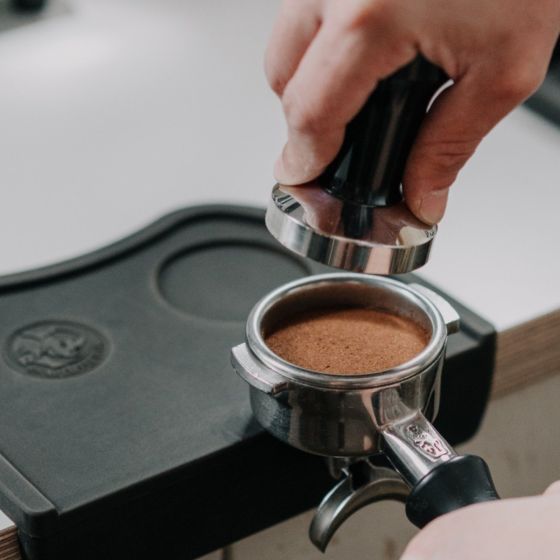 Person using a tamper to compress coffee grounds in an espresso grinder.