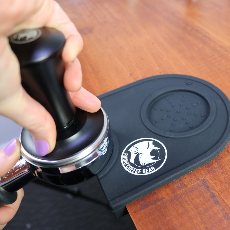 Hand using a coffee tamp with a branded tamper on a wooden surface
